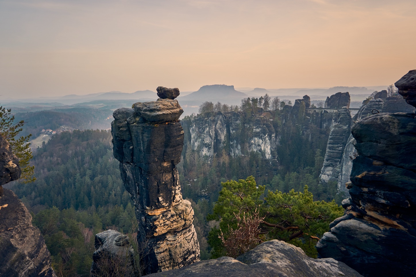 Die Felsnadel Wehlnadel vor den Sandsteinfelsen der Bastei mit der Basteibrücke, dahinter der Lilienstein im Dunst