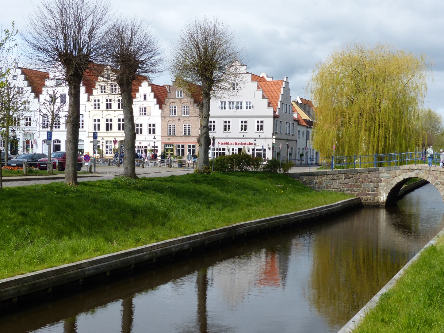 Weiße Häuser mit Treppengiebeln am Markt von Friedrichstadt, davor eine Gracht mit Steinbrücke und einer Trauerweide
