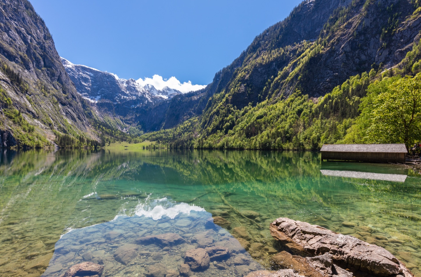 Der Obersee beim Königssee mit klarem, grünem Wasser, einem hölzernen Bootshaus und steilen Bergwänden